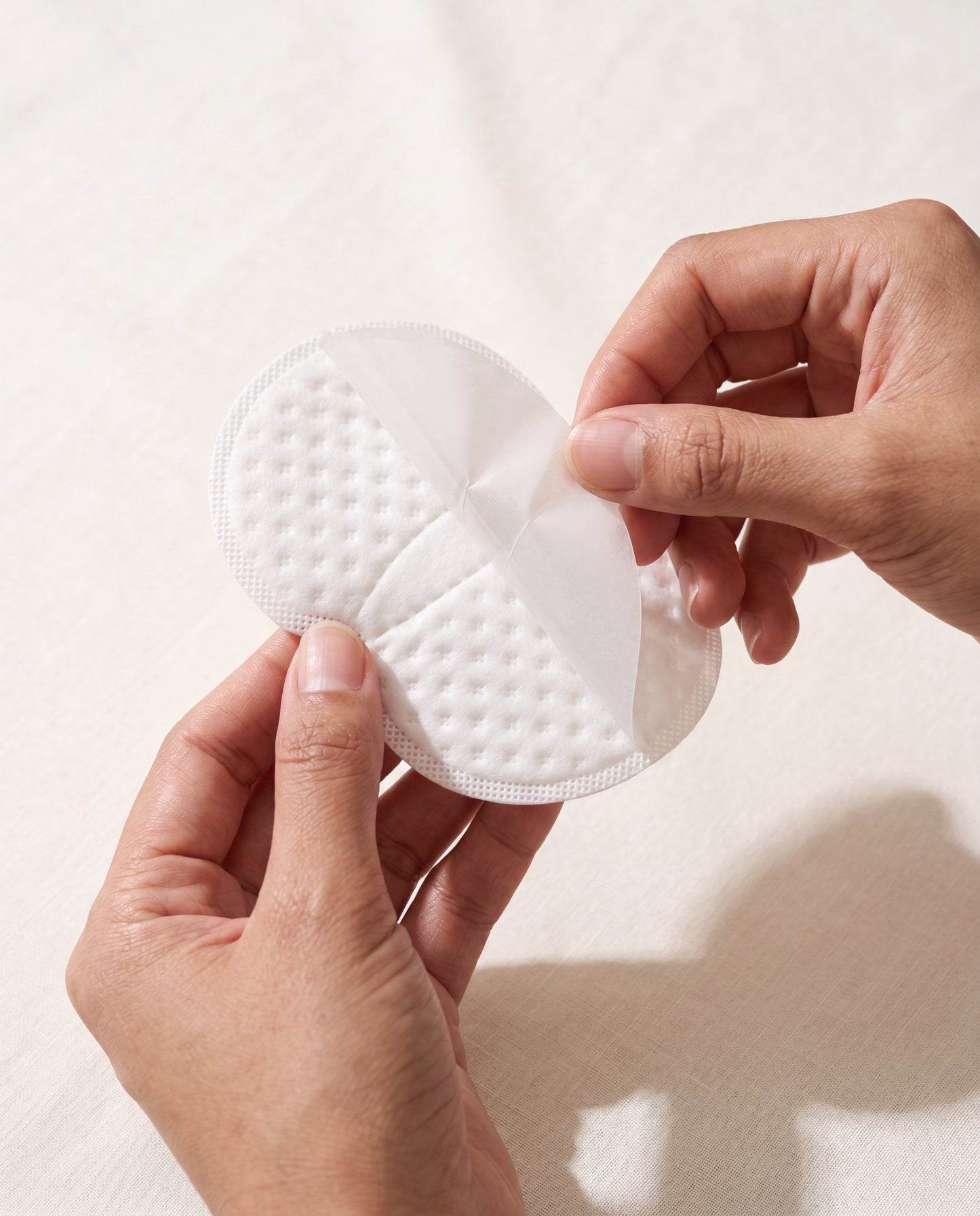 Hands peeling adhesive backing off a sweat pad