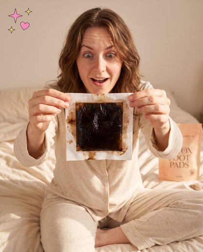 Brunette woman holding up dark stained used detox pad with surprised expression
